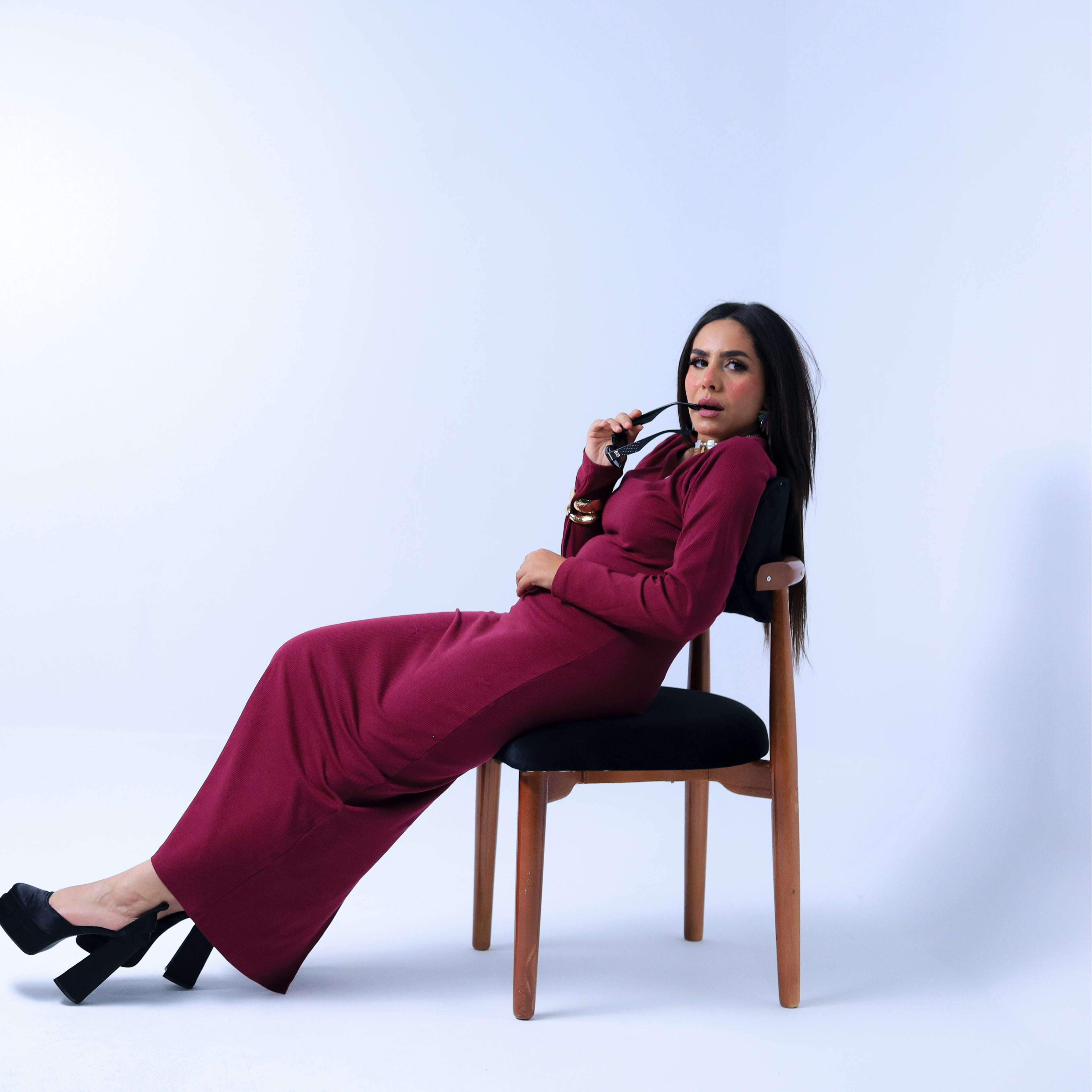 Woman in a burgundy dress sitting on a chair against a white background 
family stores